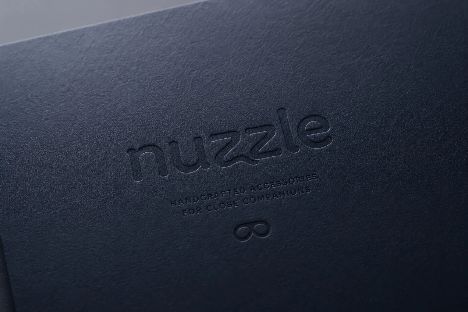 nuzzle dark blue blind embossed wordmark on textured leather paper